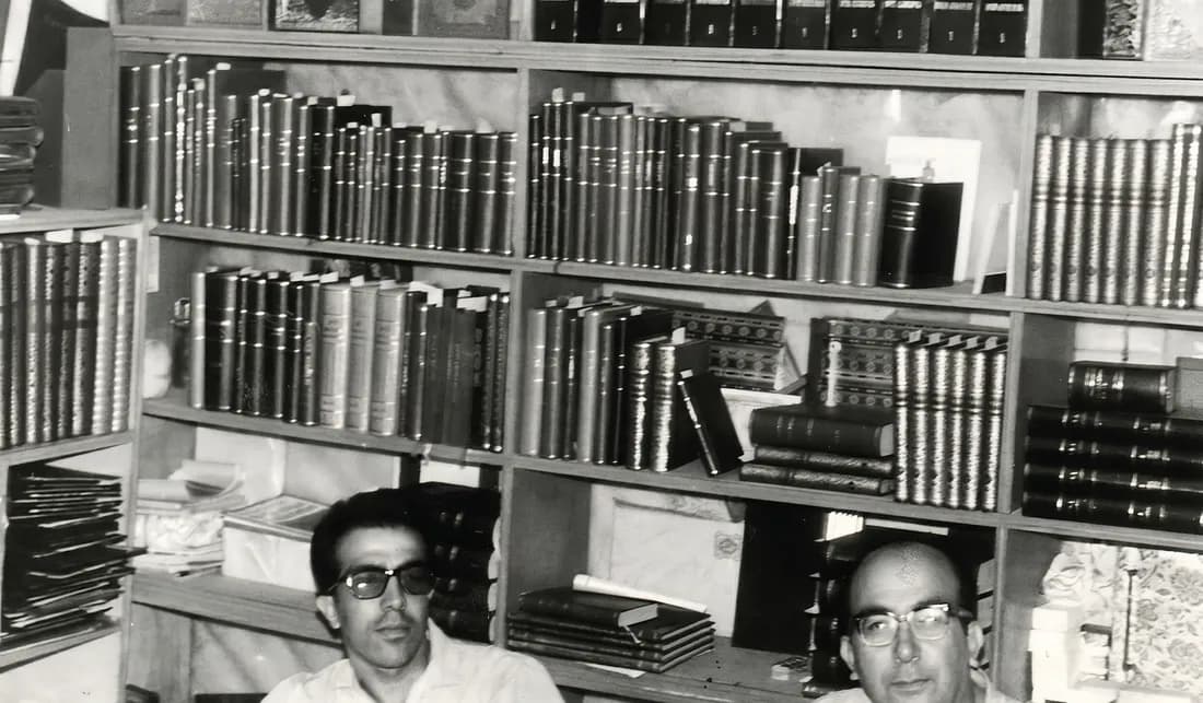 Arşivden siyah-beyaz fotoğraf: ciltli kitaplarla dolu rafların önünde gözlüklü iki adam